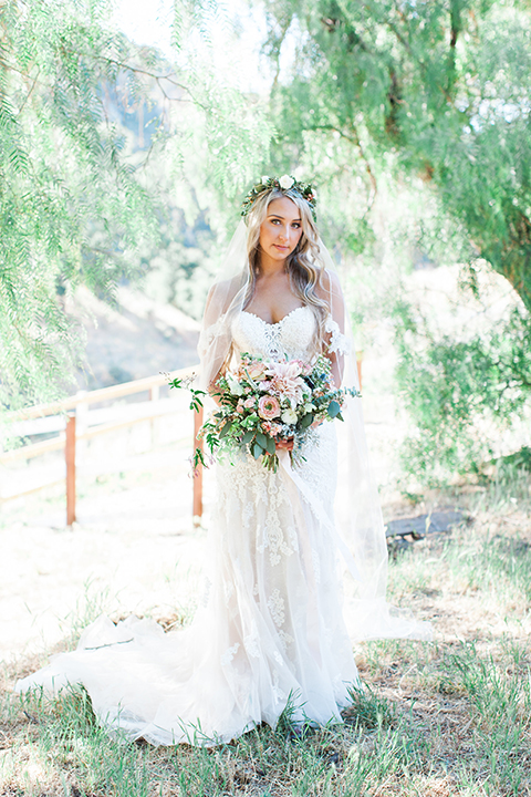 California outdoor wedding at the rancho san antonio bride form fitting lace gown with off the shoulder straps and a sweetheart neckline with a flower crown holding white and green floral bridal bouquet 