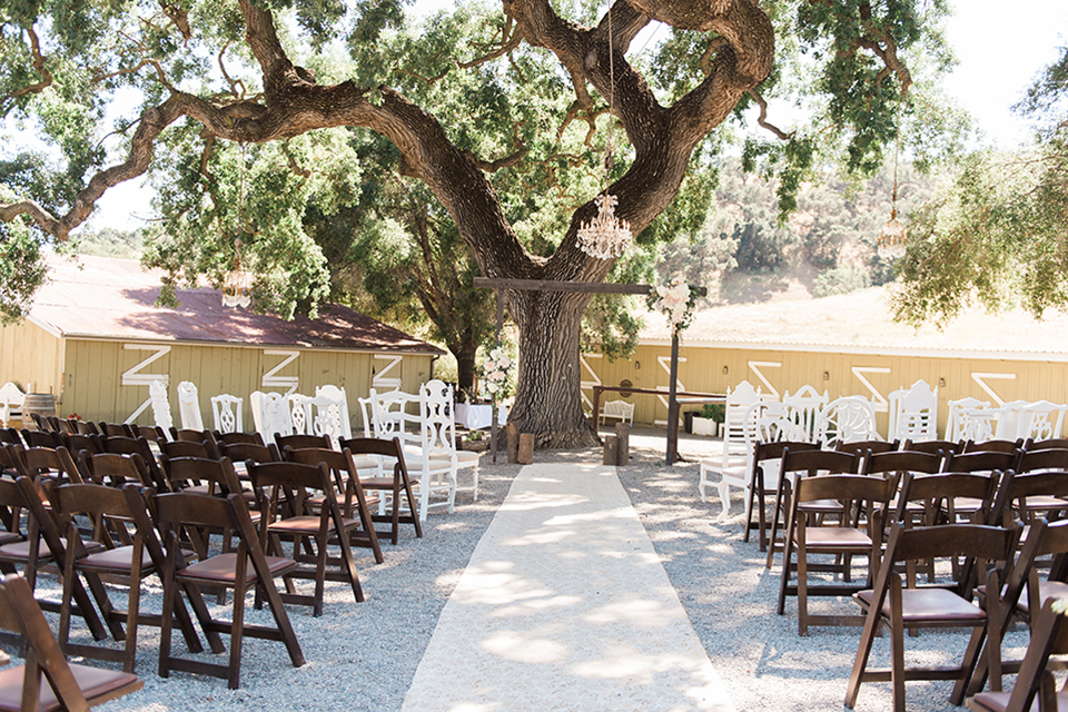 California outdoor wedding at the rancho san antonio ceremony set up white linen runner with brown and white chairs and brown wood altar with flower decor and hanging chandelier wedding photo idea for ceremony set up