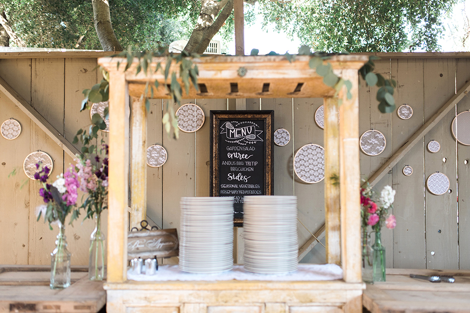 California outdoor wedding at the rancho san antonio wedding reception dinner set up with plates and black and white board for menu with wood decor and handing designs on wall with white flowers wedding photo idea for reception