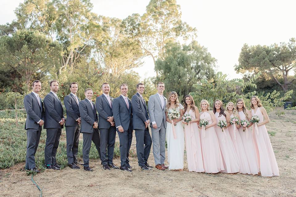 Rancho palos verdes outdoor wedding at a private estate bride a line chiffon gown with a lace bodice and short lace sleeves with a sweetheart neckline and groom heather grey notch lapel suit with a matching vest and white dress shirt with a long white tie bride holding white and green floral bridal bouquet with wedding party bridesmaids long blush pink dresses and groomsmen charcoal grey suits with long white ties