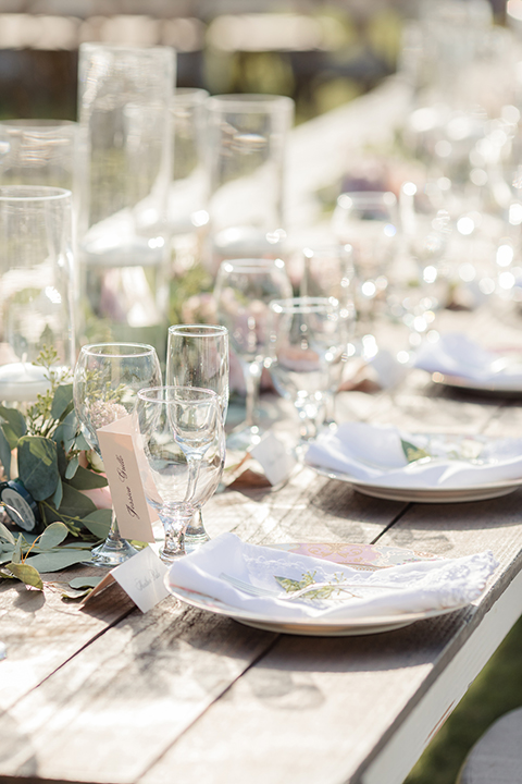 Rancho palos verdes outdoor wedding at a private estate reception set up with grey table linens and white place settings with white napkins and green floral centerpiece decor with glass vases and floating white candles with brown wood chairs and hanging light decor