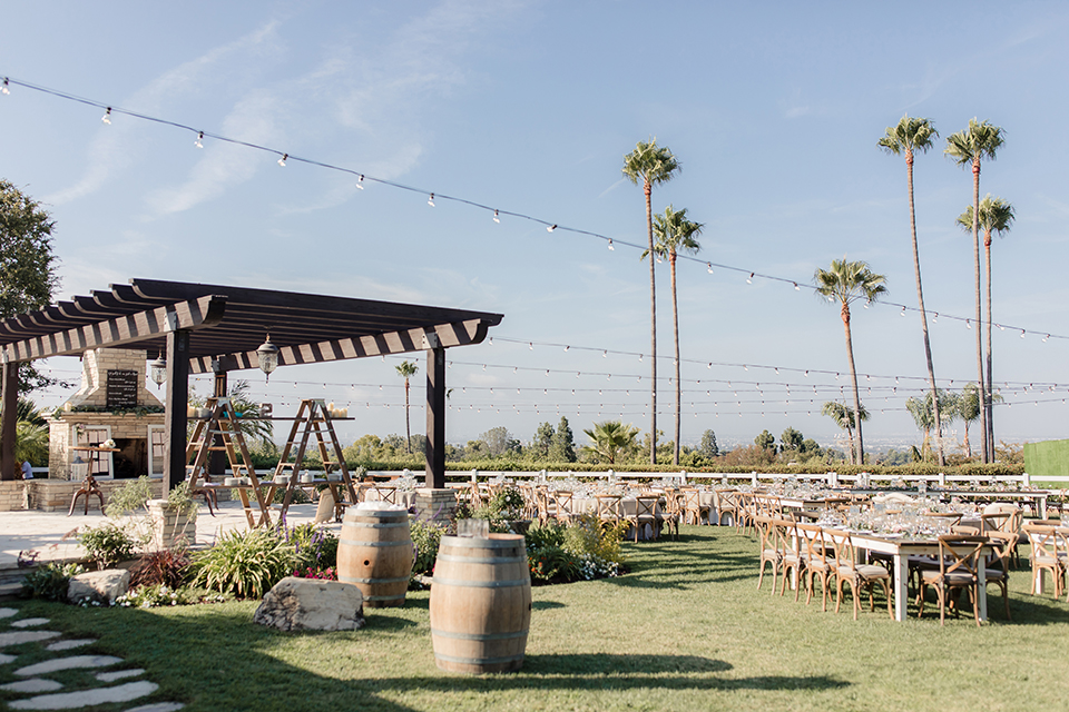 Rancho palos verdes outdoor wedding at a private estate reception set up with grey table linens and white place settings with white napkins and green floral centerpiece decor with glass vases and floating white candles with brown wood chairs and hanging light decor
