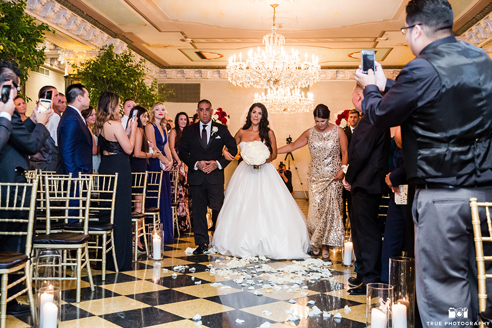 San diego glamorous wedding at the us grant hotel bride strapless ball gown with a tulle skirt and sweetheart neckline and a crystal belt with a long veil holding white floral bridal bouquet walking down the aisle with parents