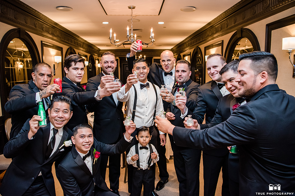 San diego glamorous wedding at the us grant hotel groom white tuxedo with black shawl lapel and black tuxedo pants with a white dress shirt and black bow tie with a white floral boutonniere with groomsmen black tuxedos with black bow ties holding drinks