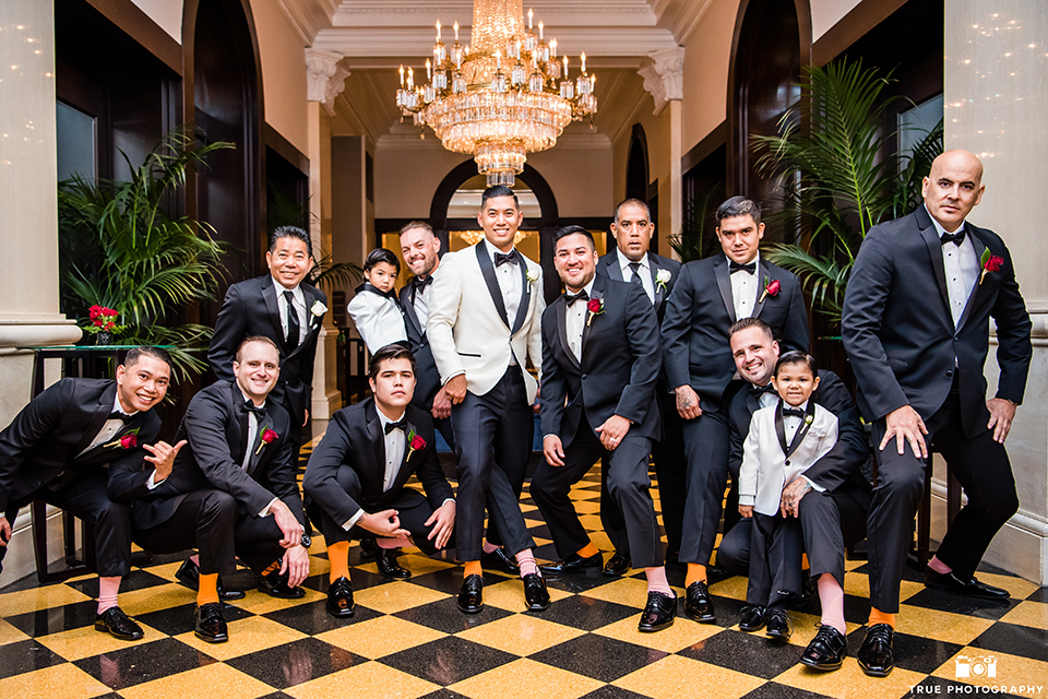 San diego glamorous wedding at the us grant hotel groom white tuxedo with black shawl lapel and black tuxedo pants with a white dress shirt and black bow tie with a white floral boutonniere with groomsmen black tuxedos with black bow ties showing socks