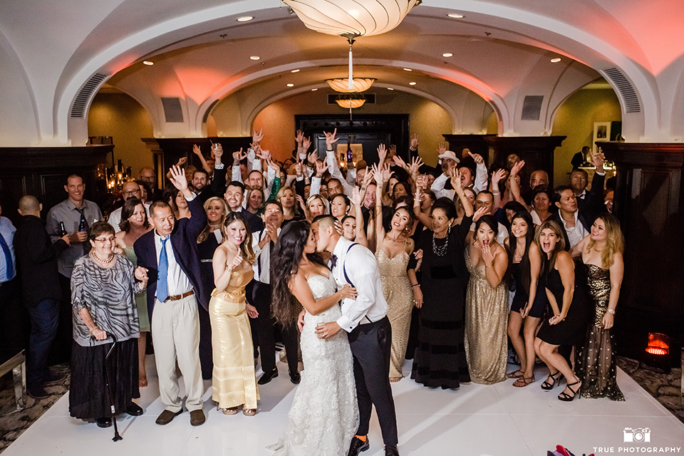 San diego glamorous wedding at the us grant hotel bride strapless ball gown with a tulle skirt and sweetheart neckline and a crystal belt with a long veil and groom white tuxedo jacket with a black shawl and black pants with a black bow tie and white floral boutonniere reception kissing with wedding guests cheering