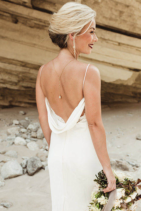 Anza-Borrego-styled-shoot-back-detail-of-bridal-gown-and-jewelry-bride-has-her-hair-up-in-a-bun-with-tear-drop-earrings-oen-back-dress-in-a-bright-bridal-white-with-straps-holding-her-bouquet