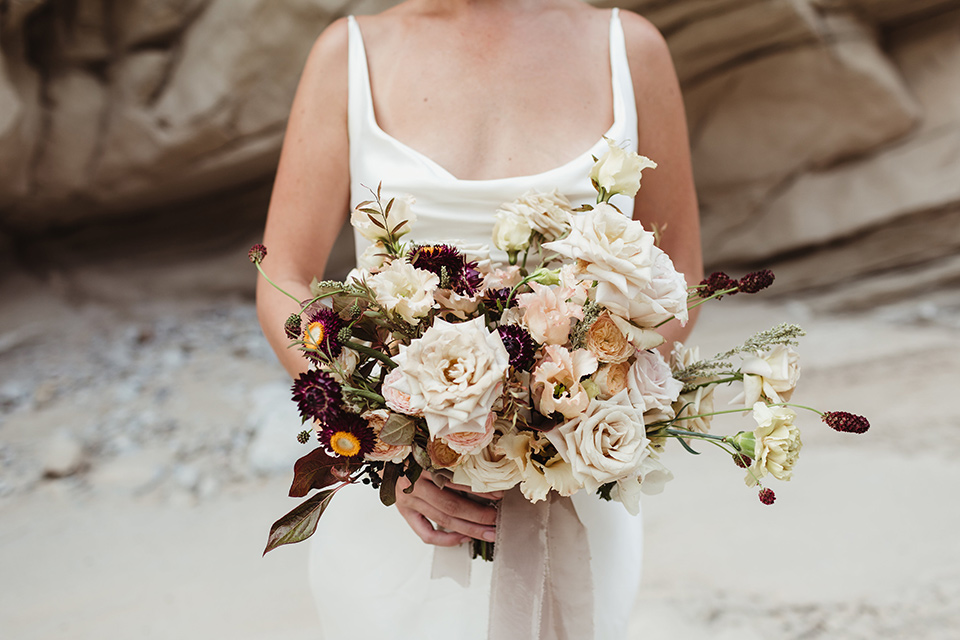 Anza-Borrego-styled-shoot-close-up-on-bridal-bouquet-big-white-flowers-with-small-red-and-green-ones-bride-holding-them-wearing-a-silk-white-gown-with-thin-straps