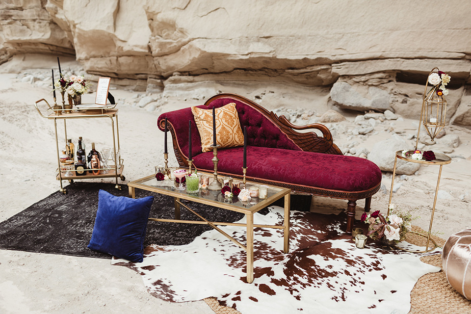 Anza-Borrego-styled-shoot-lounge-chair-and-décor-red-lounge-chair-with-gold-pillows-gold-bar-cart-with-gold-candle-holders-all-around