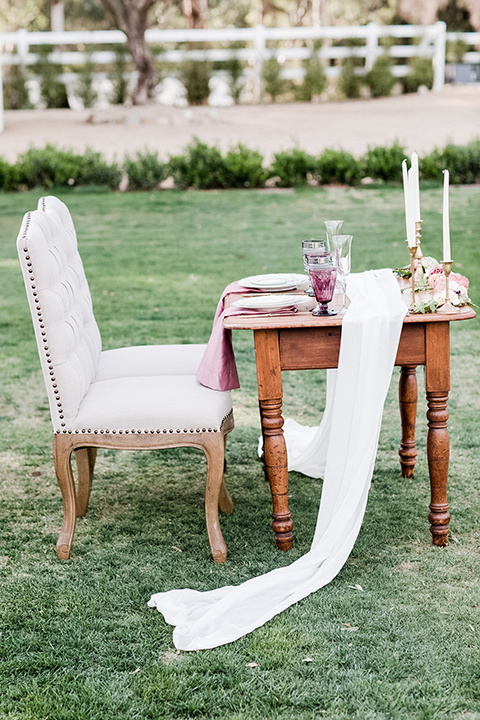 Los angeles outdoor wedding at brookview ranch table set up brown wood table with blush pink napkin decor with white place settings and tall white candles with white vintage chairs and white and pink flower decor