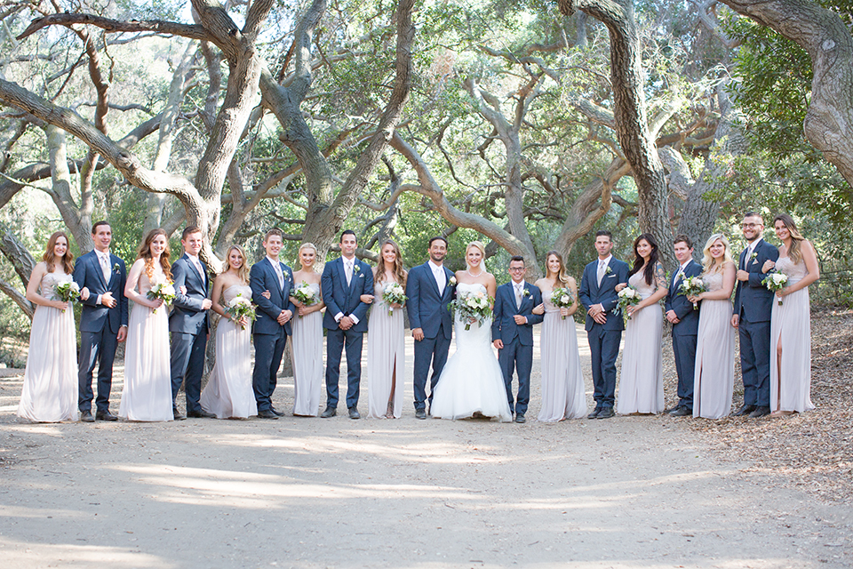 Orange county outdoor wedding at the oak canyon nature center bride form fitting mermaid style strapless gown with a crystal belt and sweetheart neckline with a long veil and groom slate blue notch lapel suit with a matching vest and white dress shirt with a long white tie and white floral boutonniere standing with wedding party bridesmaids long grey dresses and groomsmen slate blue suits with long white ties