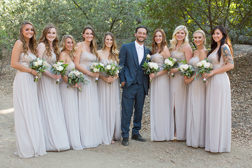 Orange county outdoor wedding at the oak canyon nature center groom slate blue notch lapel suit with a matching vest and white dress shirt with a long white tie and white floral boutonniere standing with bridesmaids long grey dresses holding white and green floral bridal bouquets