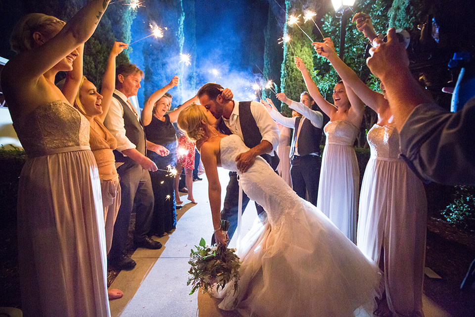 Orange county outdoor wedding at the oak canyon nature center bride form fitting mermaid style strapless gown with a crystal belt and sweetheart neckline with a long veil and groom slate blue notch lapel suit with a matching vest and white dress shirt with a long white tie and white floral boutonniere kissing after sparkler exit