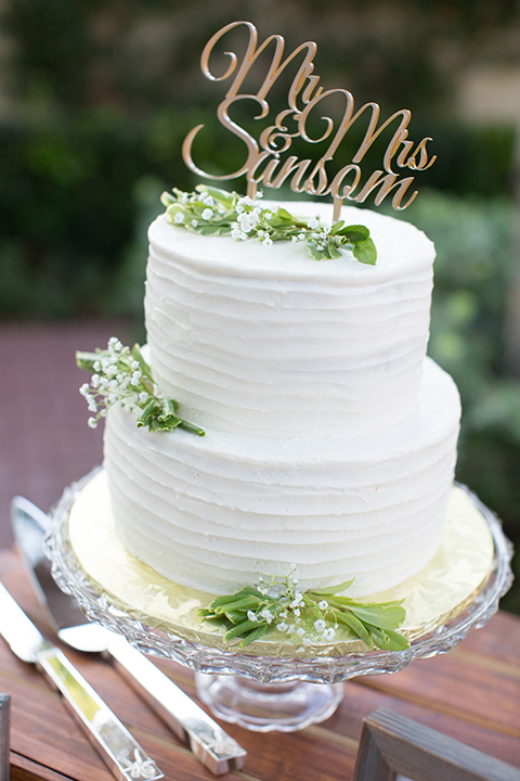 Orange county outdoor wedding at the oak canyon nature center table set up white table linen with white place settings and green and white flower centerpiece decor with dark brown chiavari chairs and candle decor two tier white wedding cake with green floral decor and gold calligraphy cake topper