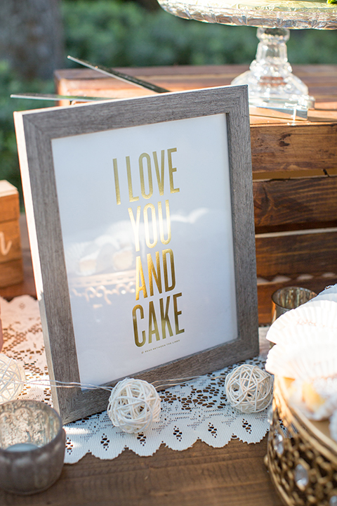 Orange county outdoor wedding at the oak canyon nature center table set up white table linen with white place settings and green and white flower centerpiece decor with dark brown chiavari chairs and candle decor and wedding cake sign on dessert table