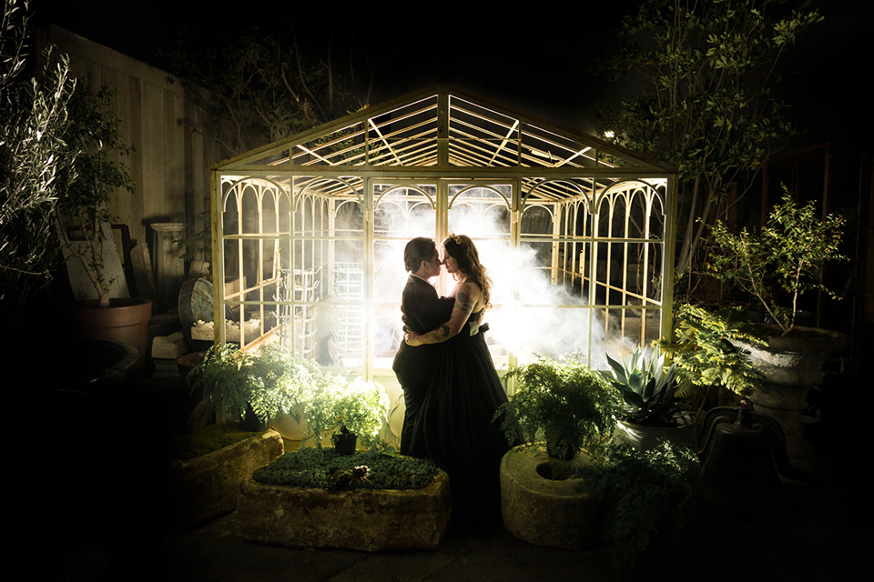 Fox and the owl wedding shot at big daddys antiques bride black womens shawl lapel tuxedo with a white dress shirt and red lace design on neckline with red floral boutonniere with bride black ball gown with thin straps and sweetheart neckline standing and hugging at night