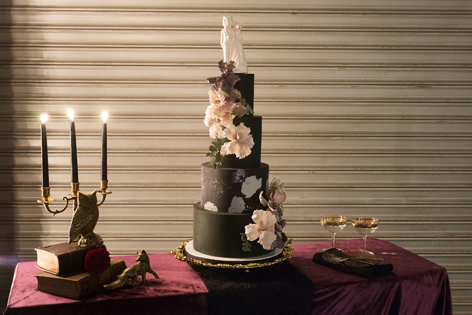 Fox and the owl wedding shoot at big daddys antiques table set up black table with white table runner and black and red place settings with tall white candles and red and pink flower centerpiece decor with tall black candles with fox and owl decor with wedding cake four tier black cake with white flower decor on side