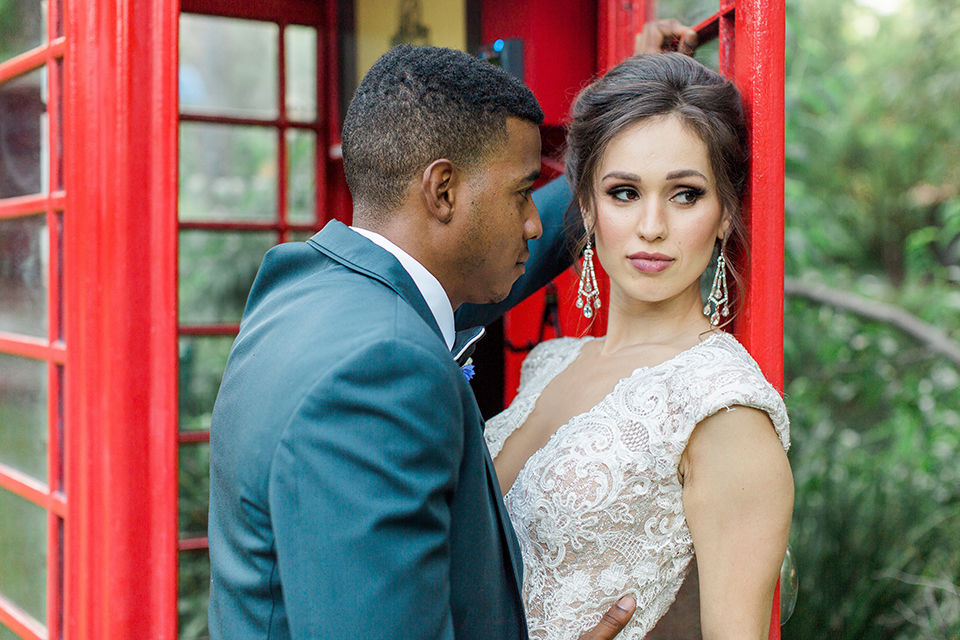 Rancho las lomas outdoor wedding shoot with spanish inspiration bride form fitting lace gown with beaded detail and a plunging neckline with open back design with groom slate blue notch lapel suit with a matching vest and white dress shirt with a matching slate pipe edge bow tie hugging in phone booth