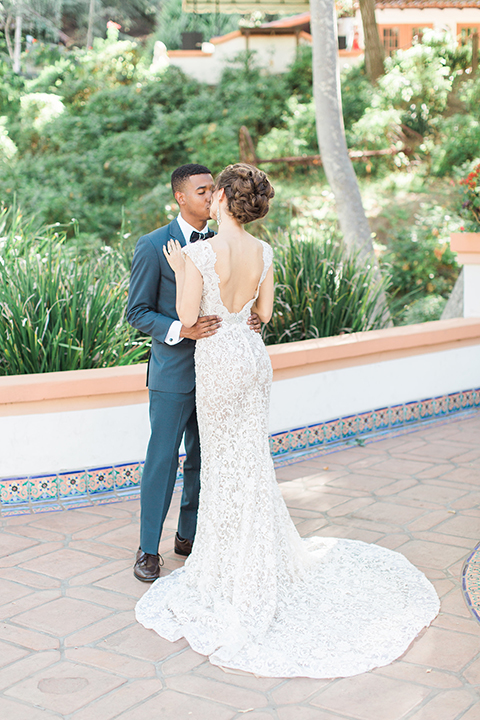 Rancho las lomas outdoor wedding shoot with spanish inspiration bride form fitting lace gown with beaded detail and a plunging neckline with open back design with groom slate blue notch lapel suit with a matching vest and white dress shirt with a matching slate pipe edge bow tie hugging and kissing