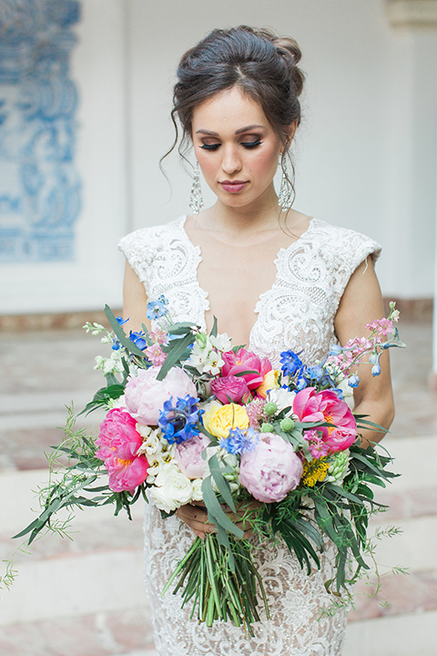 Rancho las lomas outdoor wedding shoot with spanish inspiration bride form fitting lace gown with beaded detail and a plunging neckline with open back design holding pink and blue colorful floral bridal bouquet close up