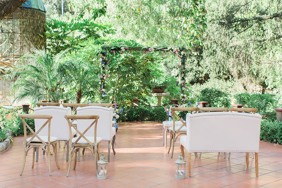 Rancho las lomas outdoor wedding with spanish inspiration wedding ceremony set up with lush greenery backdrop and wood altar with flower decor and white vintage chairs for ceremony wedding photo idea