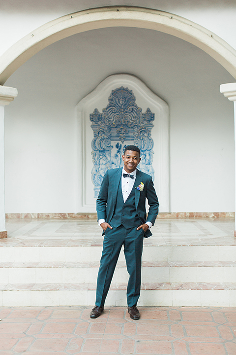 Rancho las lomas outdoor wedding with spanish inspiration groom slate blue notch lapel suit with a matching vest and white dress shirt with a matching slate blue pipe edge bow tie and white floral boutonniere