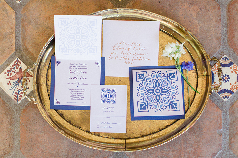 Rancho las lomas outdoor wedding with spanish inspiration wedding invitations white and blue patterned wedding invitations with blue writing and white and blue flower decor on gold tray for background wedding photo idea for wedding invitations