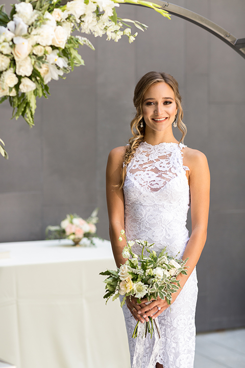 San diego wedding at the hilton bayside bride form fitting lace gown with a high halter neckline and slit in leg area standing and holding white and green floral bridal bouquet close up