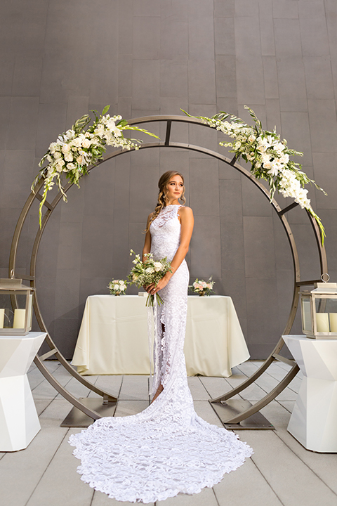 San diego wedding at the hilton bayside bride form fitting lace gown with a high halter neckline and slit in leg area standing and holding white and green floral bridal bouquet