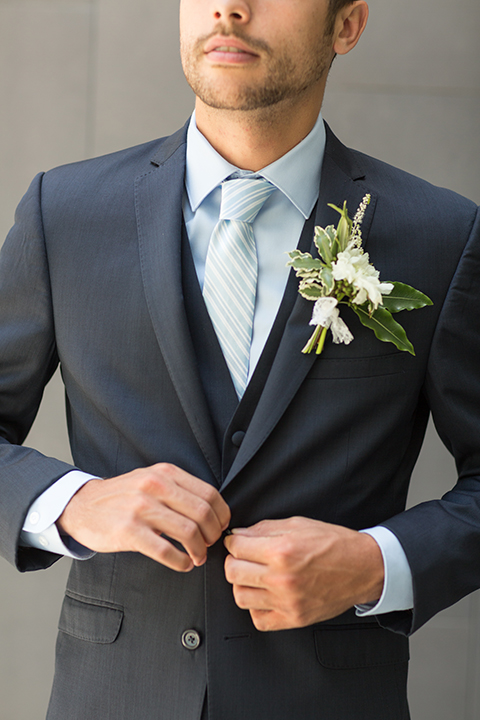 San diego wedding at the hilton bayside groom navy notch lapel suit with a matching vest and light blue dress shirt with a matching light blue long striped tie with a white and green floral boutonniere close up