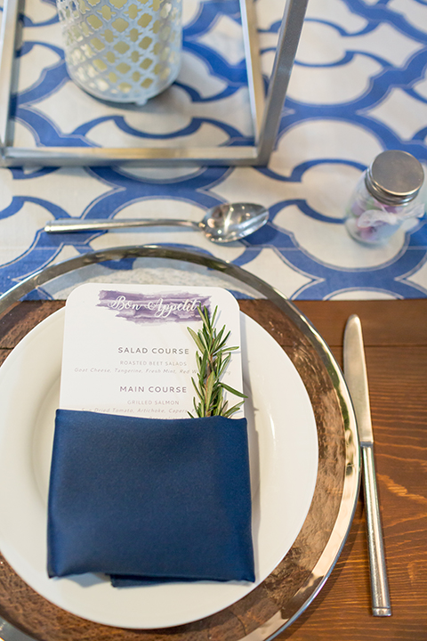 San diego wedding at the hilton bayside table set up brown wood table with white and clear place settings with blue linen napkin decor and white and blue table runner with white and green tall flower centerpiece decor in clear vases with white chiavari chairs