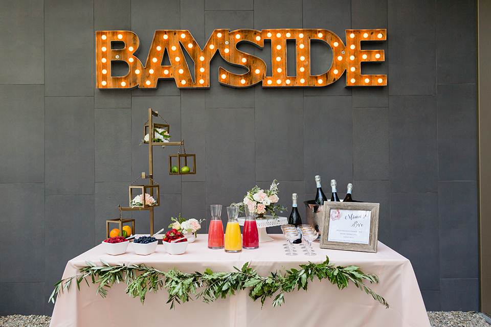 San diego wedding at the hilton bayside table set up with blush pink table linen and white chiavari chairs with white place settings and silver linen napkin decor with short white and green flower centerpiece decor with glassware and silverware with drinks and light up sign 