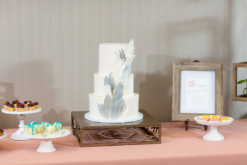 San diego wedding at the hilton bayside table set up with blush pink table linen and white chiavari chairs with white place settings and silver linen napkin decor with short white and green flower centerpiece decor with glassware and silverware with wedding cake three tier white cake with grey design and flower decor