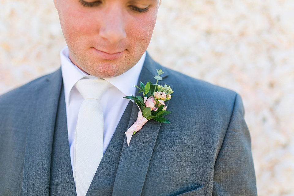 Temecula outdoor wedding at bel vino winery groom grey notch lapel suit with a matching vest and white dress shirt with a long white tie and white and pink floral boutonniere close up