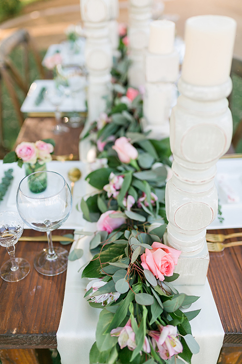 Temecula outdoor wedding at bel vino winery table set up dark brown wood table with white square place settings and pink and green garland flower decor in center and gold silverware decor with matching brown chairs and white table runner