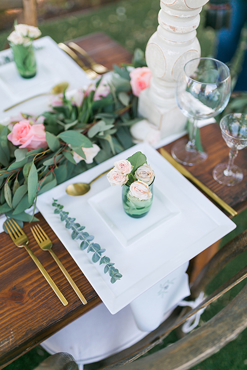 Temecula outdoor wedding at bel vino winery table set up dark brown wood table with white square place settings and pink and green garland flower decor in center and gold silverware decor with matching brown chairs and white table runner