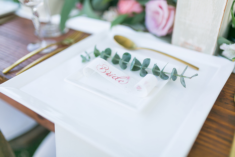 Temecula outdoor wedding at bel vino winery table set up dark brown wood table with white square place settings and pink and green garland flower decor in center and gold silverware decor with matching brown chairs and white table runner