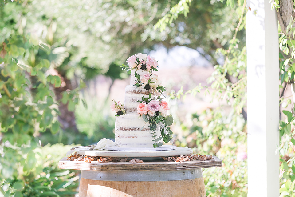 Temecula outdoor wedding at bel vino winery wedding cake three tier white bare wedding cake with pink and green flower decor on side with white tray on wine barrel wedding photo idea for wedding cake