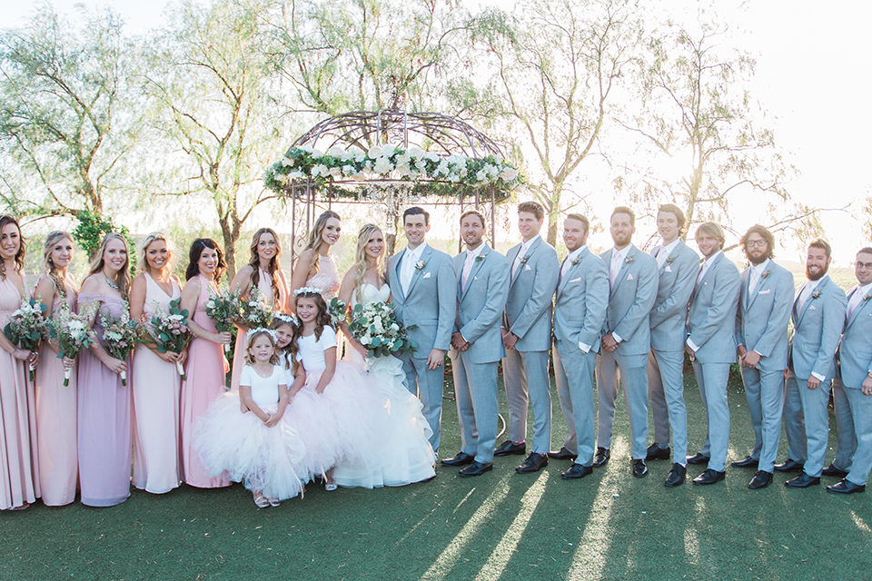 Temecula outdoor wedding at falkner winery bride mermaid style gown with lace bodice and sweetheart neckline with ruffled skirt and long veil with groom heather grey suit with white dress shirt and long white tie with matching pocket square and white floral boutonniere with bridesmaids long blush pink dresses holding white and green floral bridal bouquets and groomsmen heather grey suits with long white ties