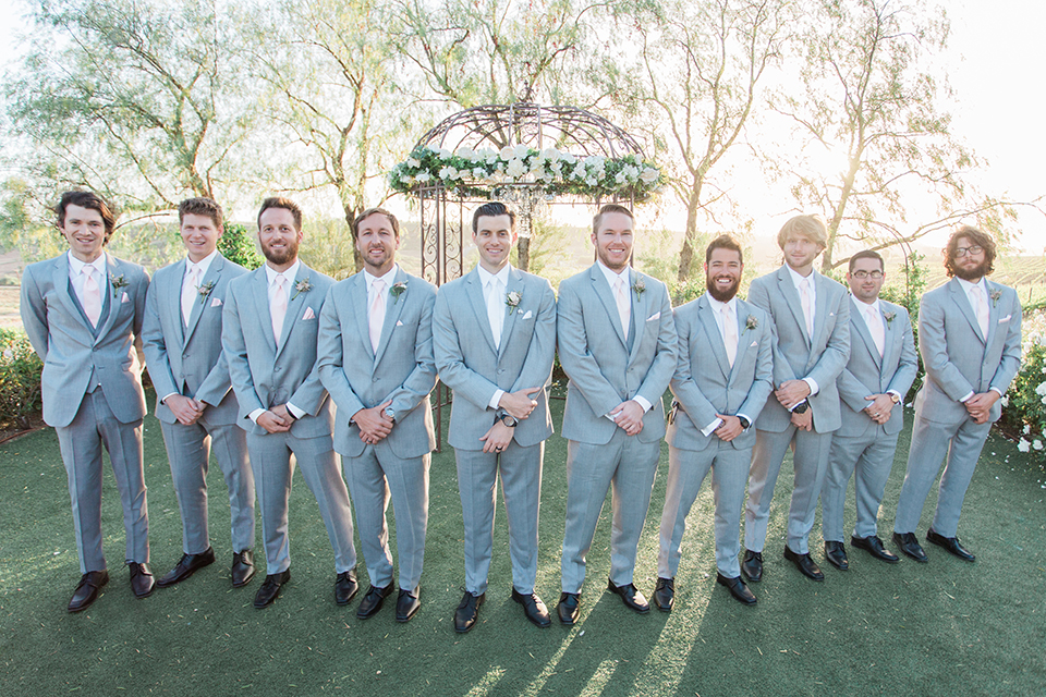 Temecula outdoor wedding at falkner winery groom heather grey suit with white dress shirt and long white tie with matching pocket square and white floral boutonniere with groomsmen heather grey suits with long white ties