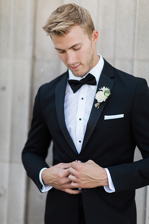 Boutonniere style black notch lapel tuxedo with a black bow tie and a simple white floral boutonniere front view