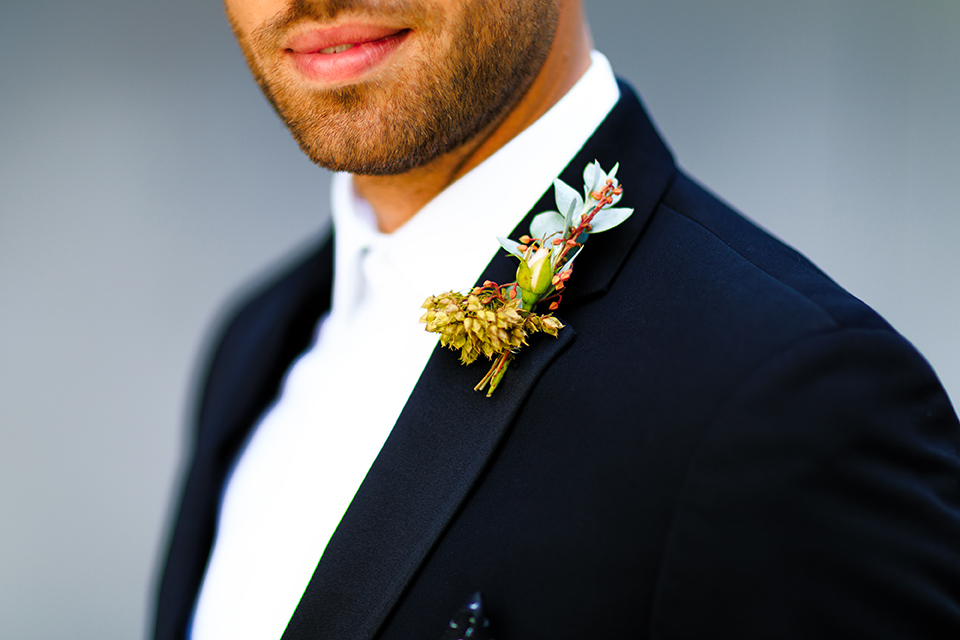 Boutonniere style black notch lapel tuxedo with a white long tie and greenery floral boutonniere