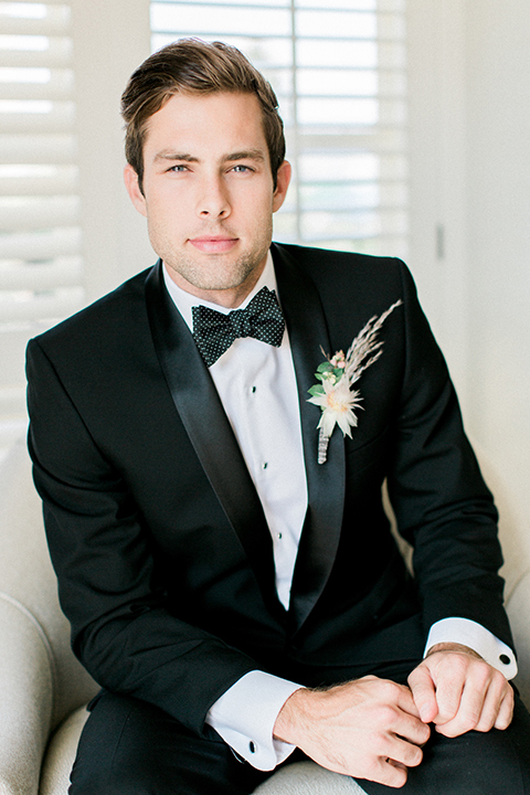 Boutonniere-style-black-shawl-lapel-tuxedo-with-a-black-and-white-dot-bow-tie-and-large-floral-boutonniere