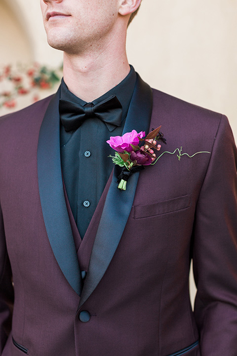 Boutonniere-style-burgundy-shawl-lapel-tuxedo-with-a-black-shirt-and-black-bow-tie-with-a-pink-floral-boutonniere