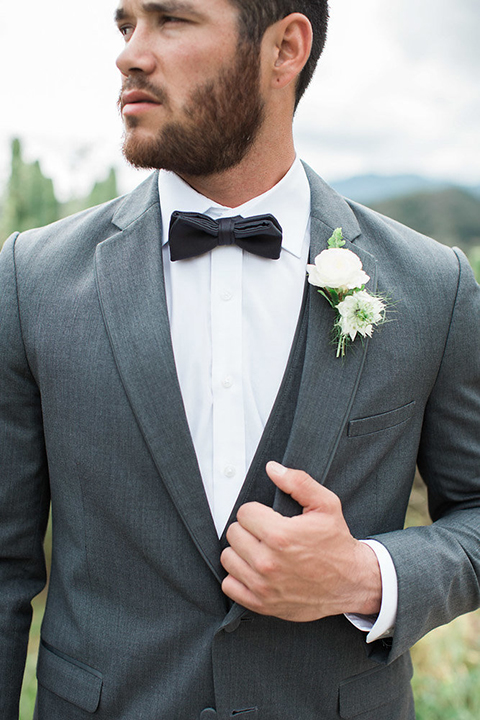 Boutonniere-style-charcoal-grey-notch-lapel-suit-with-a-black-bow-tie-and-white-floral-boutonniere