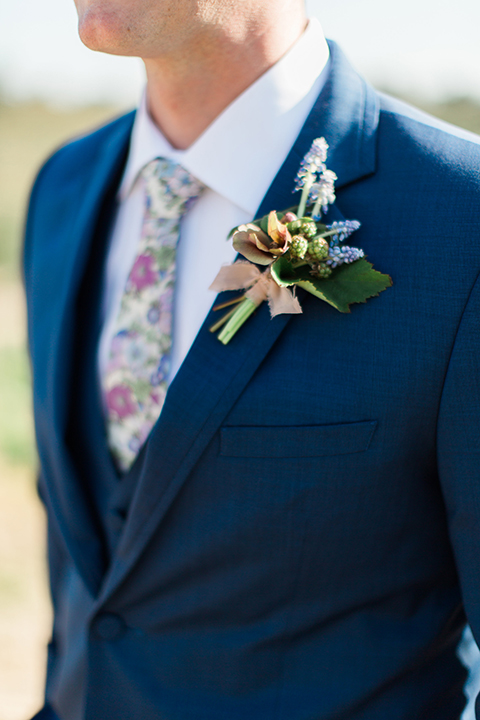 Boutonniere-style-cobalt-blue-notch-lapel-suit-with-a-white-floral-tie-and-greenery-and-blue-floral-boutonniere