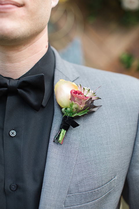 Boutonniere-style-grey-notch-lapel-suit-with-a-black-shirt-and-black-bow-tie-with-a-white-and-pink-floral-boutonniere