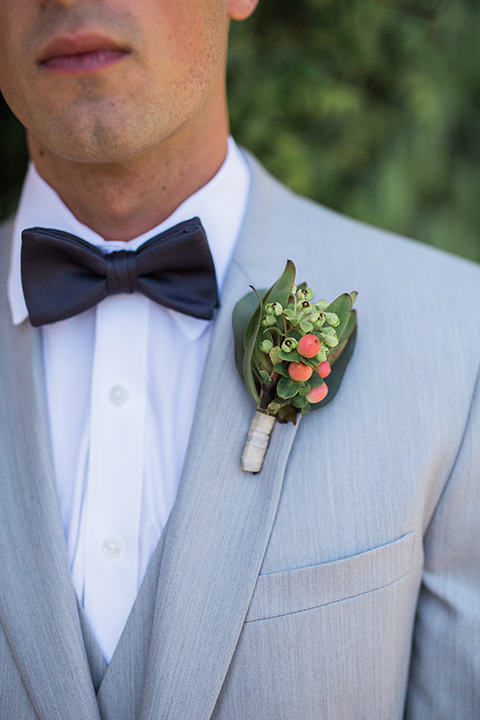 boutonniere style light grey peak lapel suit with a charcoal grey bow tie and a green boutonniere