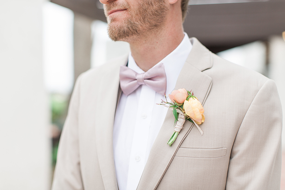 Boutonniere-style-tan-notch-lapel-suit-with-a-blush-pink-bow-tie-and-light-yellow-and-orange-floral-boutonniere