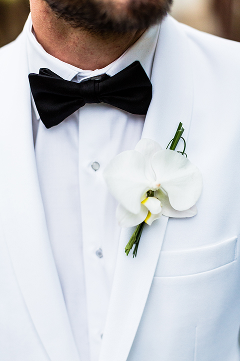 Boutonniere-style-white-notch-lapel-dinner-jacket-with-a-black-bow-tie-and-white-floral-boutonniere